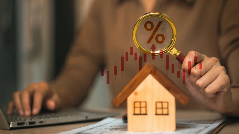 Entenda como as taxas de juros afetam o mercado imobiliário e o seu planejamento financeiro para a compra de um imóvel Pessoa analisando taxas de juros imobiliários com lupa e gráfico de mercado