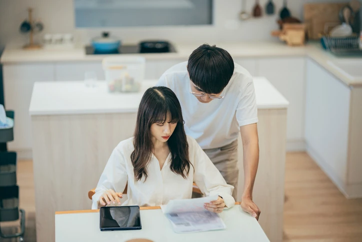 Casal jovem focado na organização das finanças domésticas utilizando tablet e documentos em uma cozinha funcional Casal jovem analisando documentos e tablet em uma cozinha moderna