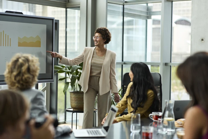 Mulher de negócios apresentando gráficos em uma tela digital durante reunião corporativa com equipe.