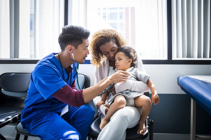 Médico pediatra examinando uma criança pequena no colo da mãe em um consultório médico