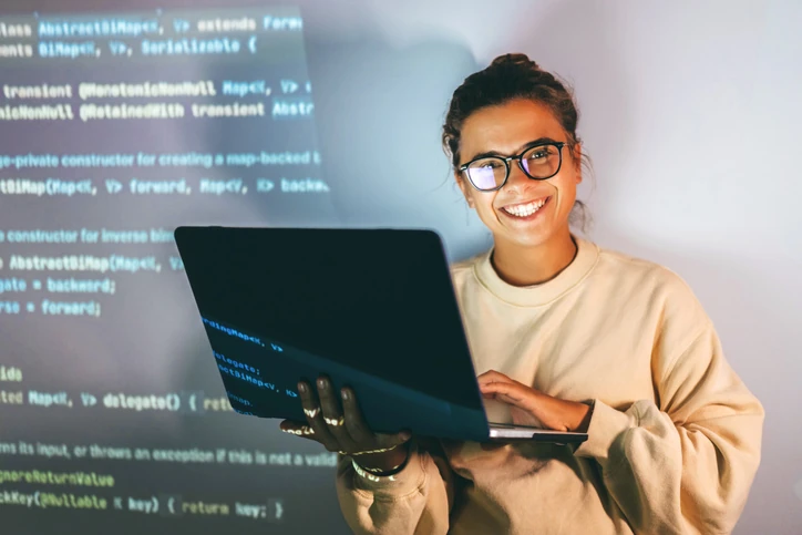 Programadora sorridente trabalhando em um notebook com código de software projetado no fundo