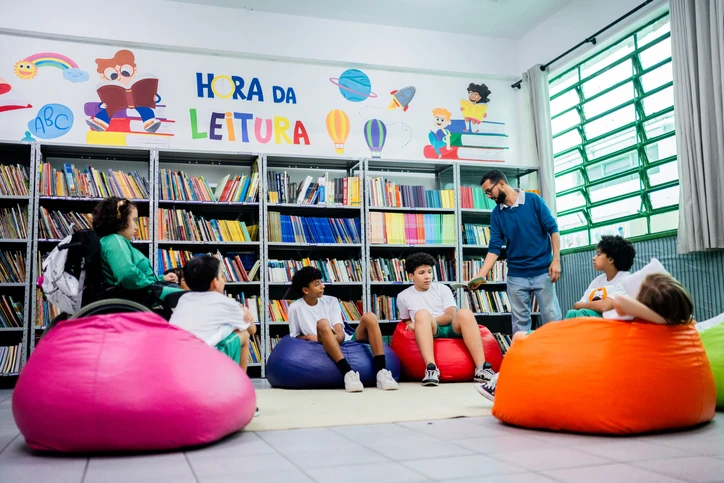 Professor e alunos em biblioteca escolar colorida durante momento de leitura