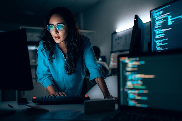 Programadora trabalhando intensamente em código de computador durante a noite em escritório moderno