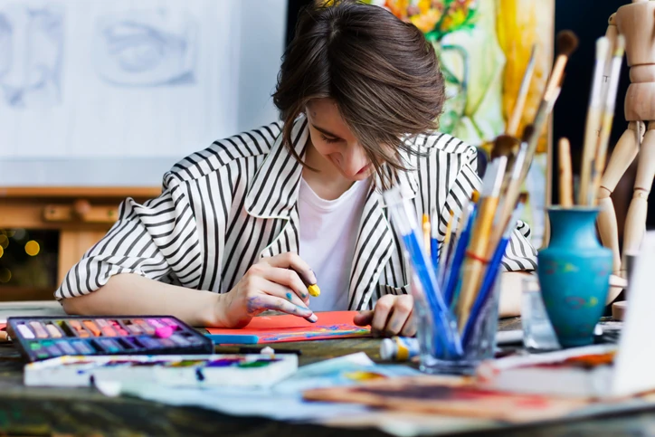 Jovem artista trabalhando em projeto de arte com materiais de pintura em um ateliê criativo