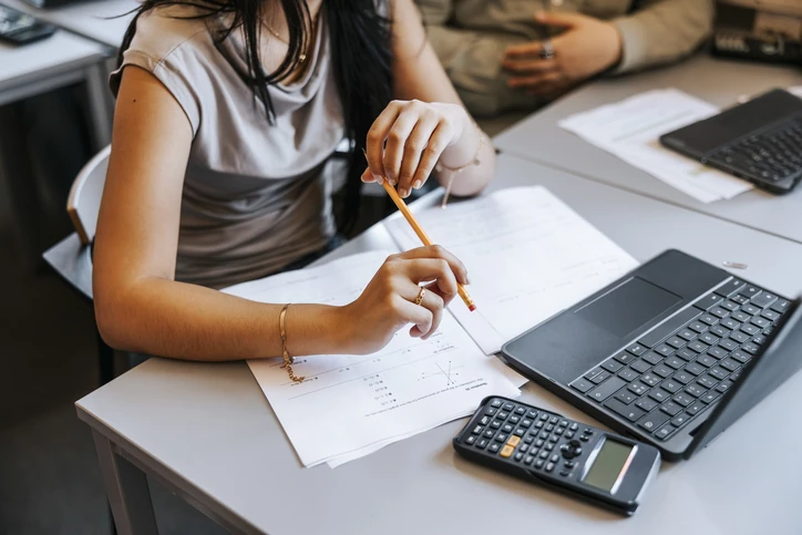 Estudante universitária utilizando calculadora e notebook para resolver problemas acadêmicos complexos em sala de aula