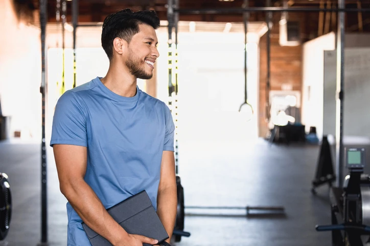 Personal trainer sorrindo em uma academia segurando um tablet