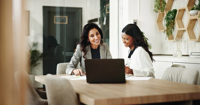 Duas mulheres profissionais colaborando em um laptop em um ambiente de escritório moderno, focado em trabalho em equipe e produtividade corporativa