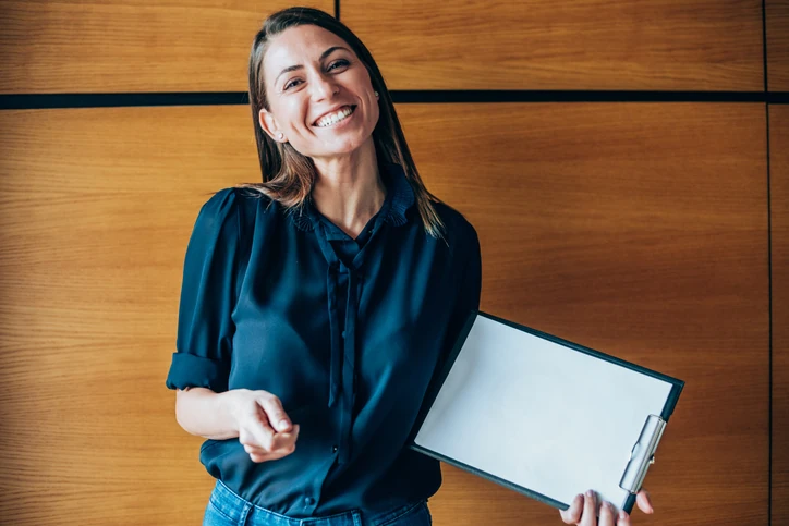 Mulher profissional sorridente segurando uma prancheta com espaço para texto em ambiente corporativo