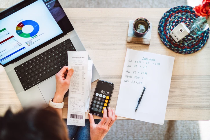 Pessoa organizando despesas mensais com laptop, calculadora e recibos