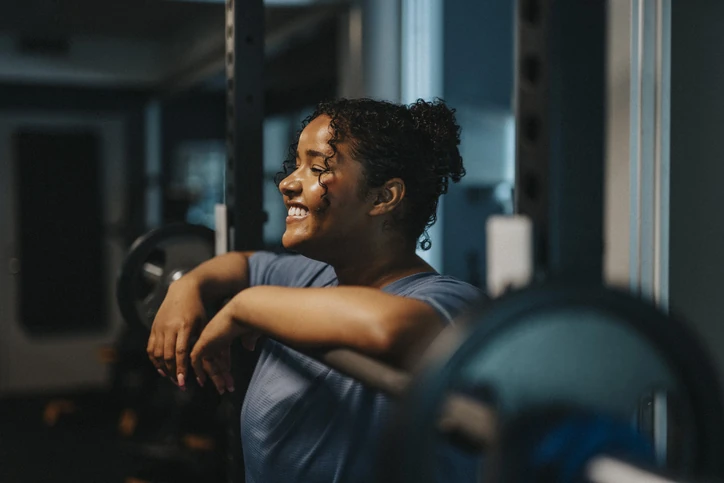 Mulher negra sorridente descansando após exercício de musculação na academia