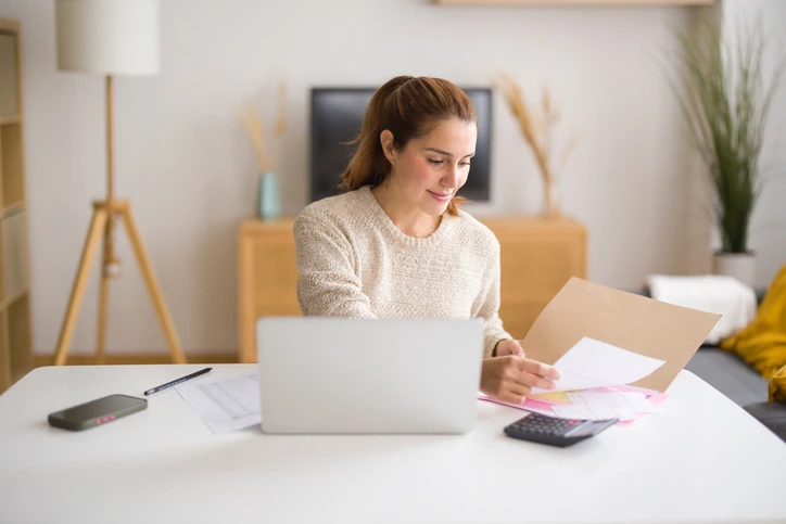 Mulher organizando finanças pessoais e documentos de trabalho no home office com notebook e calculadora