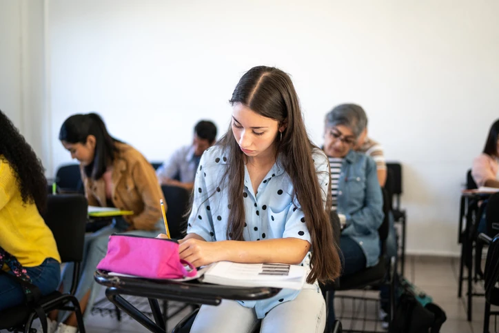 Aluna dedicada concentrada em seus estudos durante uma aula presencial em ambiente acadêmico