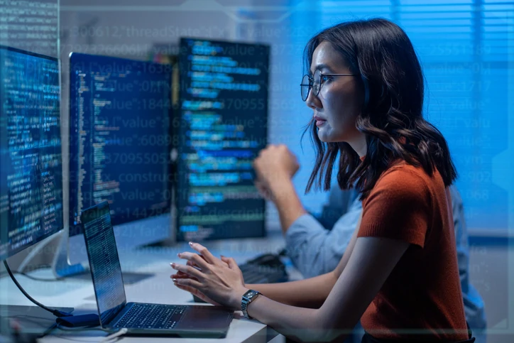 Programadora trabalhando em múltiplos monitores com códigos de software em um ambiente de escritório moderno