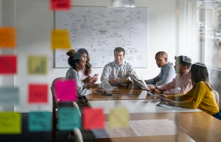 Equipe de negócios colaborando em um plano de ação com notas adesivas e quadro branco em um ambiente corporativo profissional