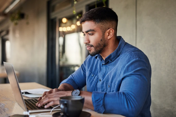 Profissional jovem focado trabalhando remotamente em seu computador portátil com café em um ambiente inspirador