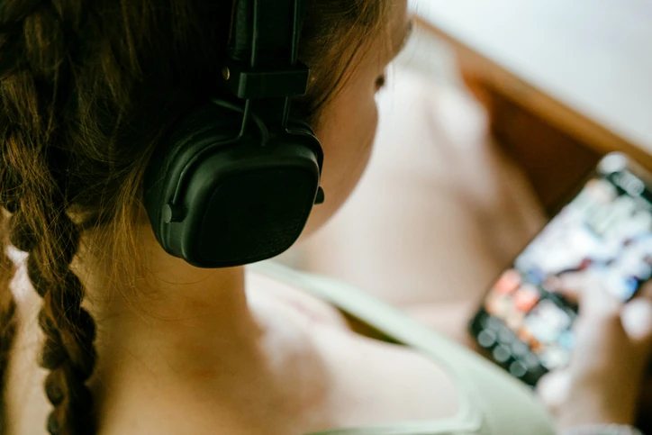 Jovem mulher utiliza fones de ouvido e smartphone para consumir conteúdo digital, música ou cursos online