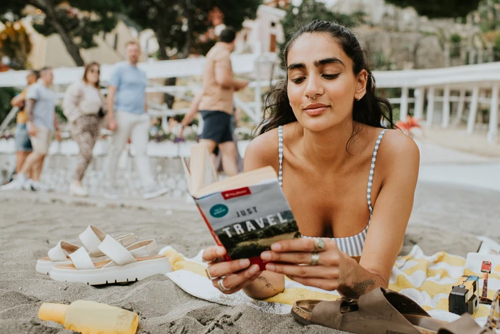 Mulher relaxando e lendo livro de viagens na praia em um dia ensolarado de férias de verão