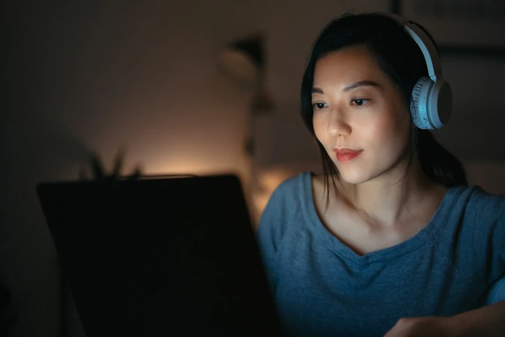 Estudante ou profissional focada utilizando laptop e fones de ouvido em ambiente noturno para atividades acadêmicas ou trabalho remoto