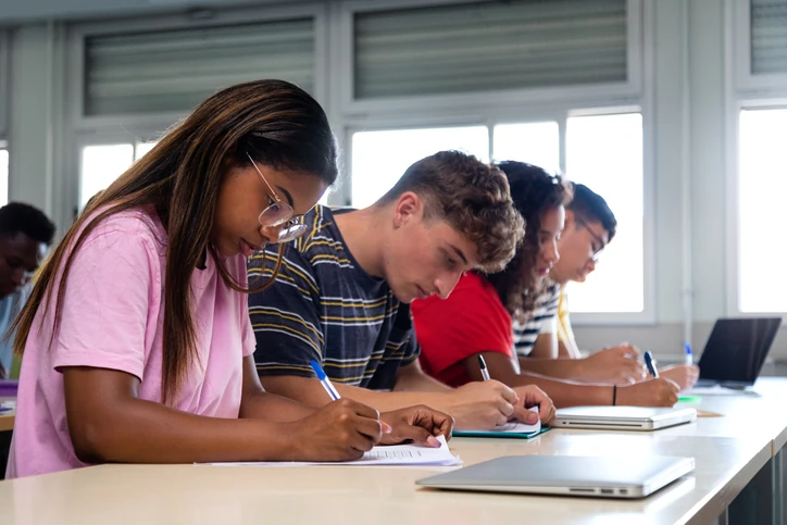 Grupo de estudantes diversos focados escrevendo em uma sala de aula