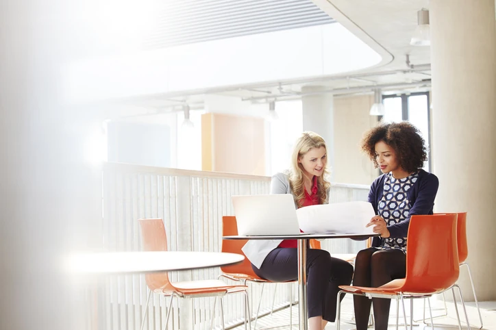 Duas mulheres profissionais colaborando em um projeto em um escritório moderno com laptop