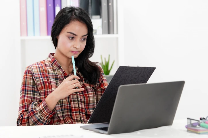 Estudante ou profissional focada analisando documentos e usando notebook no escritório