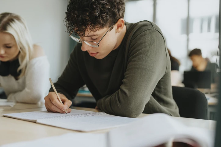Estudante focado escrevendo em um caderno em sala de aula ou biblioteca