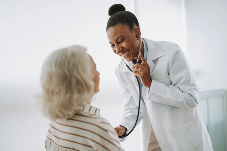 Atendimento médico humanizado: médica sorridente realizando exame clínico em paciente idosa no consultório Médica sorridente examinando uma paciente idosa com estetoscópio em consultório