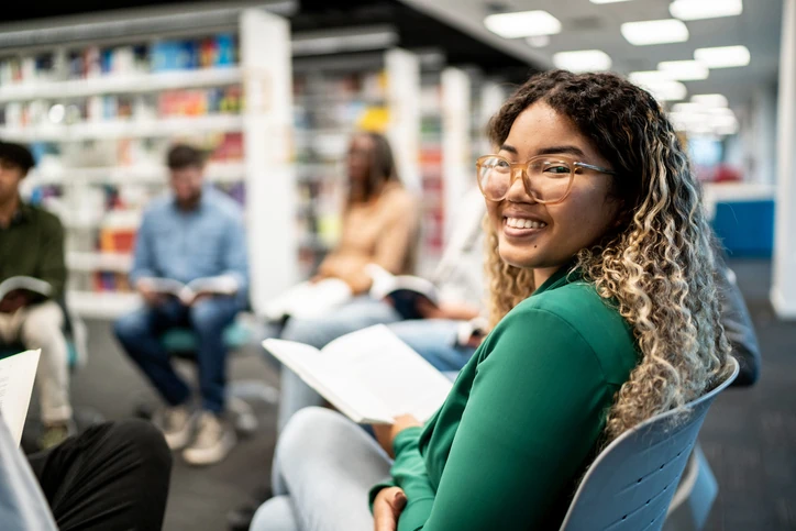 Estudante universitária sorridente participando de um grupo de leitura e estudo colaborativo em uma biblioteca moderna
