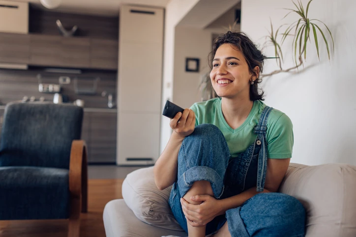 Jovem mulher descontraída assistindo televisão e relaxando confortavelmente no sofá de casa durante o tempo livre