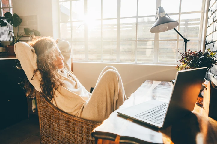 Mulher relaxando em uma cadeira confortável em um home office ensolarado com seu laptop