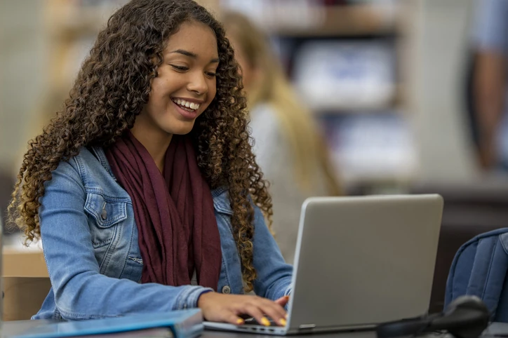 Estudante universitária focada estudando online com seu computador portátil em uma biblioteca Estudante jovem e sorridente usando laptop em ambiente acadêmico