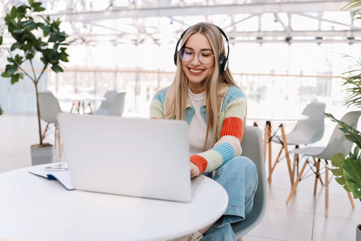 Estudante sorridente usando fones de ouvido e notebook em um ambiente de estudo moderno