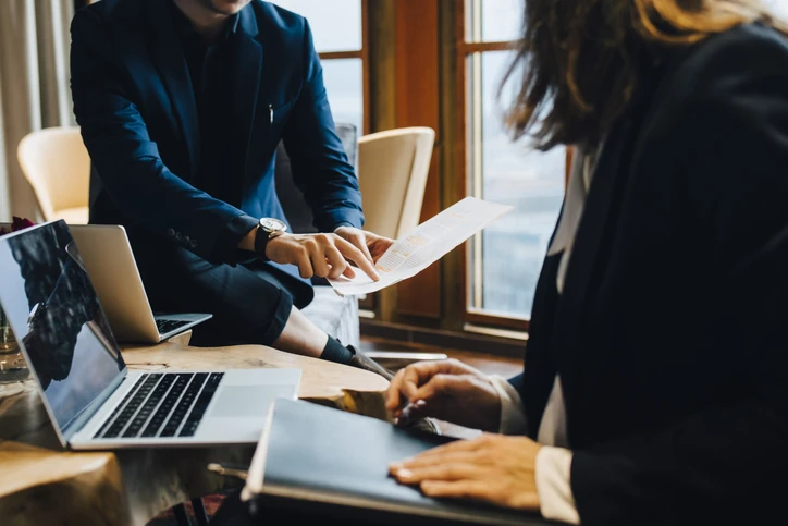 Reunião de negócios colaborativa com profissionais revisando documentos e utilizando laptops em um ambiente de escritório moderno Profissionais de negócios discutindo documentos em uma reunião de trabalho corporativa