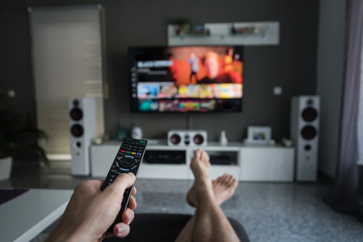 Pessoa segurando controle remoto assistindo a serviço de streaming na televisão em casa