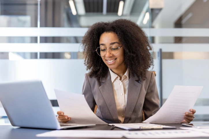 Profissional feminina focada analisando documentos e utilizando computador em ambiente de escritório corporativo moderno
