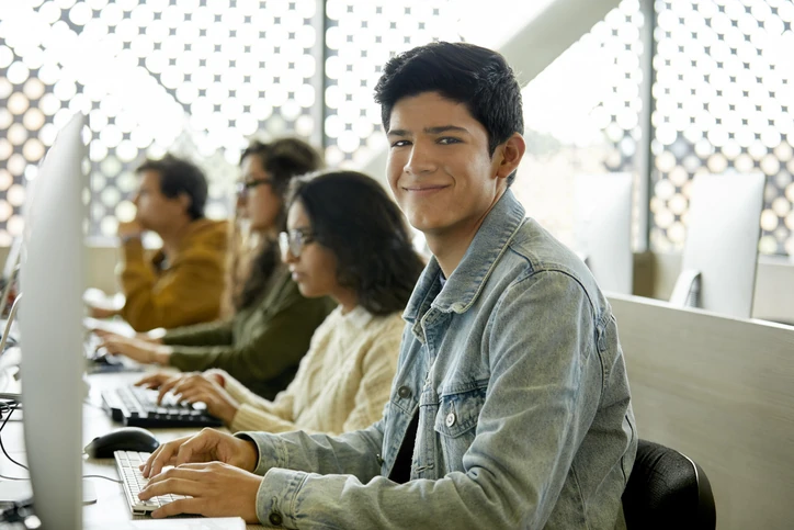 Estudante jovem sorrindo em laboratório de informática com colegas ao fundo