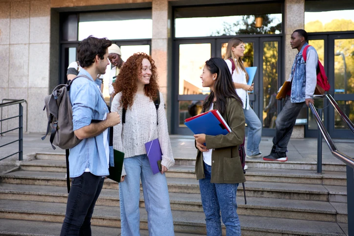 Grupo de estudantes diversos conversando na entrada de um campus universitário