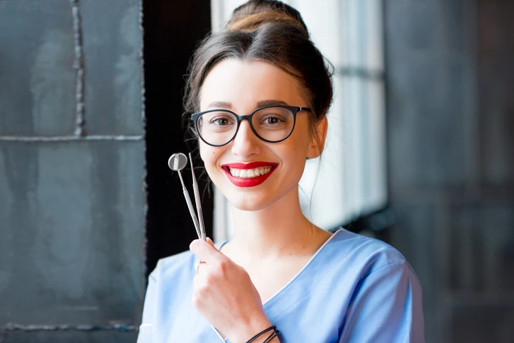 Dentista sorridente segurando instrumentos odontológicos em um consultório