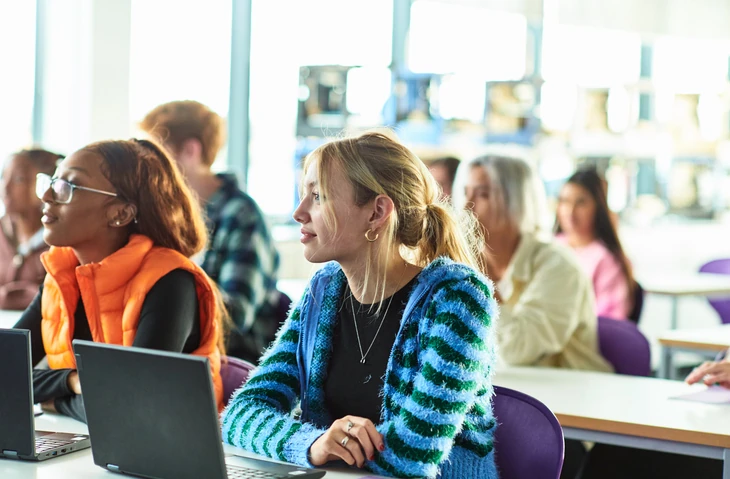 Estudantes universitários focados em aula interativa usando notebooks em sala de aula iluminada