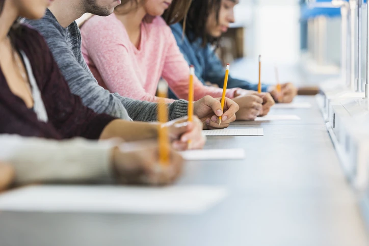Estudantes universitários focados escrevendo em uma prova durante uma avaliação acadêmica em sala de aula
