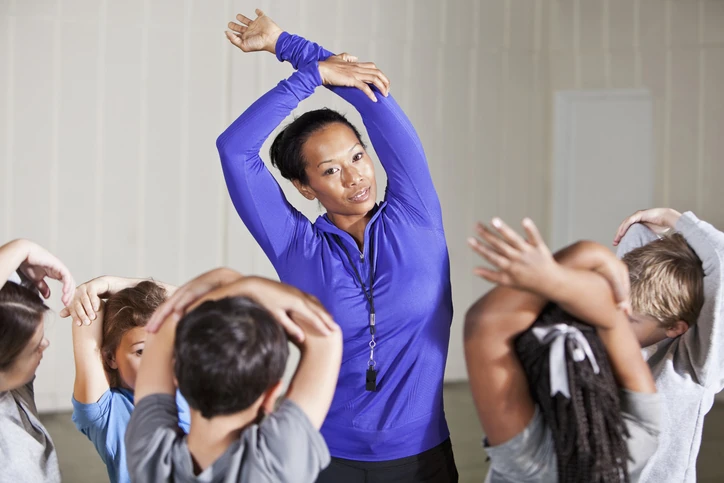 Professora de educação física orientando alunos em uma aula prática de alongamento para promover saúde e bem-estar infantil