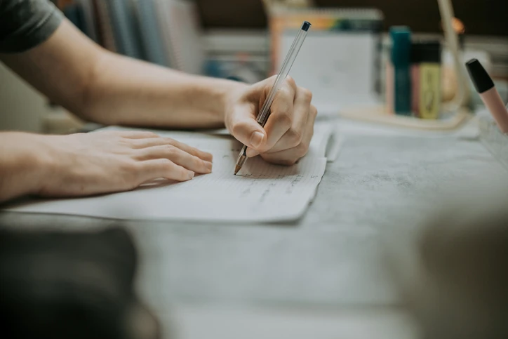 Pessoa escrevendo em caderno com caneta esferográfica em mesa de estudos Pessoa escrevendo em caderno com caneta esferográfica em mesa de estudos