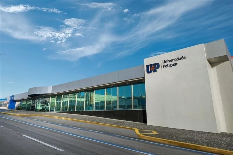 Fachada da Universidade Potiguar (UnP), com prédio moderno de paredes brancas e grandes janelas de vidro sob um céu azul.