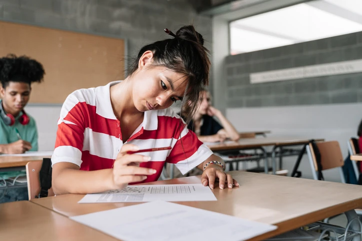 Estudante fazendo prova em sala de aula, concentrada enquanto responde questões em uma folha. Estudante fazendo prova em sala de aula, concentrada enquanto responde questões em uma folha.