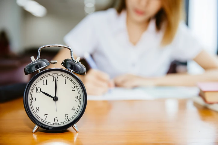 Estudante focada realizando a prova do ENEM com um relógio sobre a mesa. Estudante focado gerenciando o tempo durante o primeiro dia de prova do ENEM.