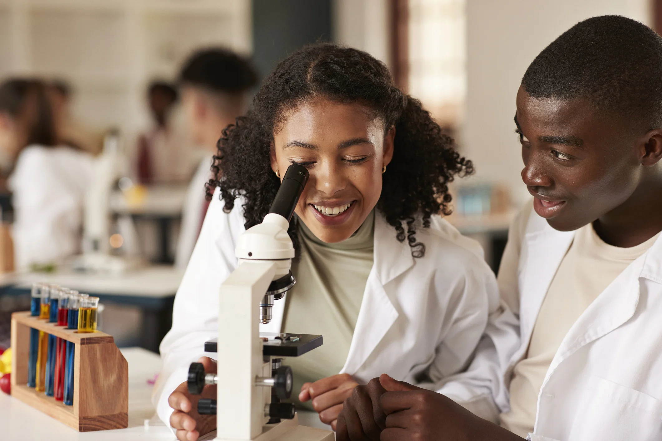 Estudantes universitários de ciência sorrindo enquanto usam um microscópio em um laboratório de química