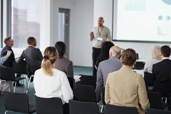 Palestrante ministrando workshop ou conferência para profissionais em sala de treinamento corporativo com projeção de slides
