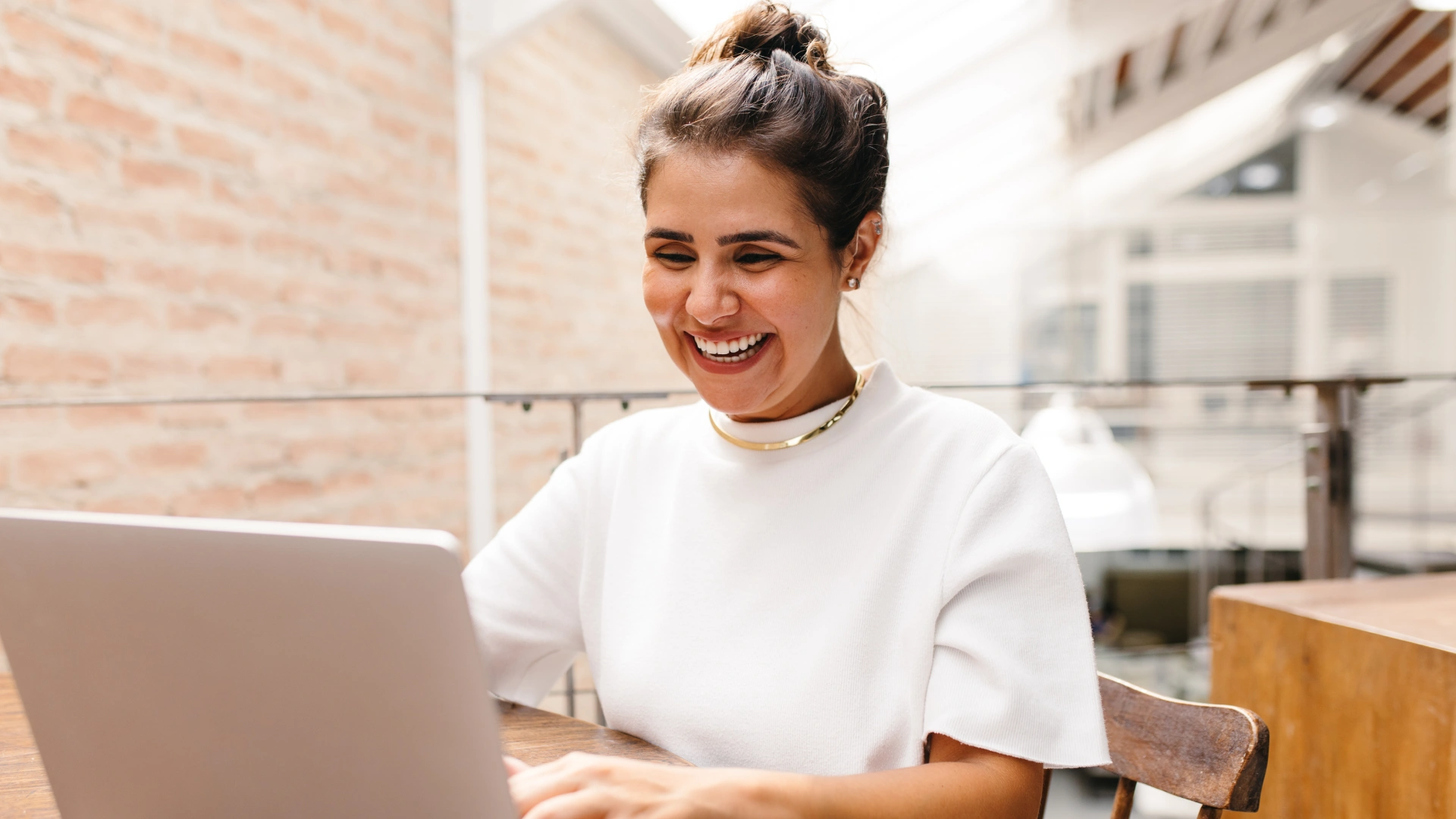 Mulher feliz utilizando notebook para trabalho ou estudos em ambiente corporativo moderno e iluminado