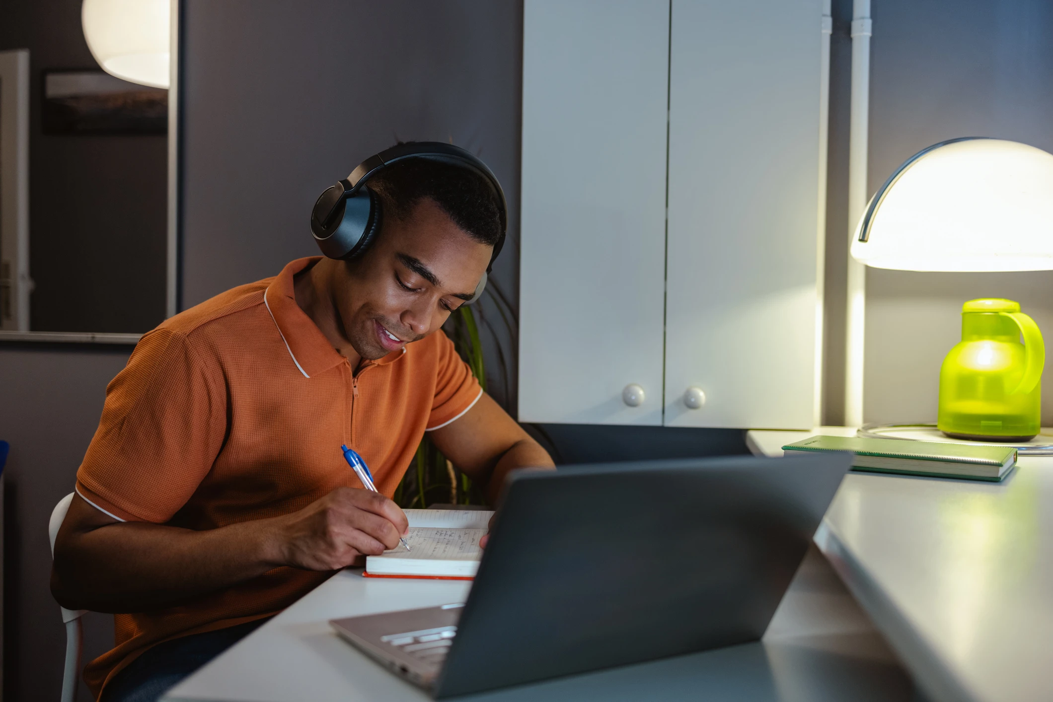 Estudante jovem usando fones de ouvido e anotando em um caderno enquanto estuda online no laptop