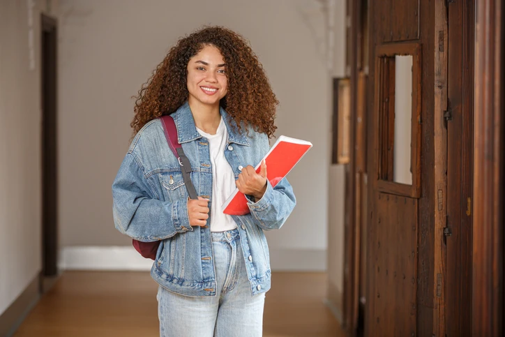 Estudante universitária sorridente segurando cadernos em um corredor escolar